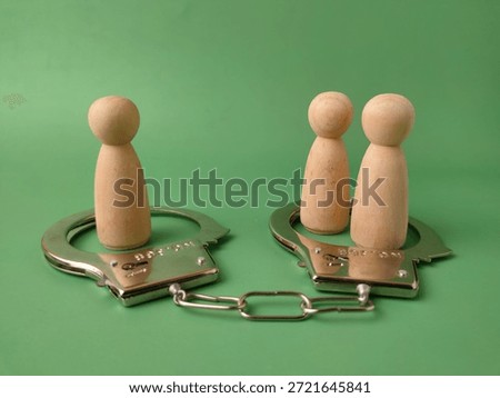 The handcuffs symbolize authority, control, and the consequences of wrongdoing, while the two separate wooden figures represent individuals or perhaps a couple facing these issues individually or jointly.