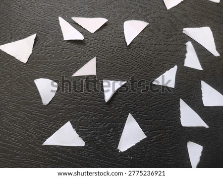 Hand-cut triangular white paper confetti pieces scattered randomly on a dark textured background