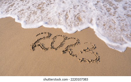 Hand-drawn numbers 2023 of new year on wet yellow sand on beach, copy space. - Shutterstock ID 2220107383