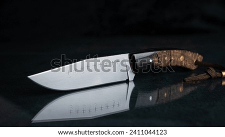 A hand-forged knife with a black horn handle on black glass, which mirrors the knife