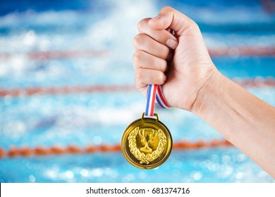 Handful Of Asian Man Holding Gold Medal With Blurry Background Of Swimming Pool And Swimming Competition.