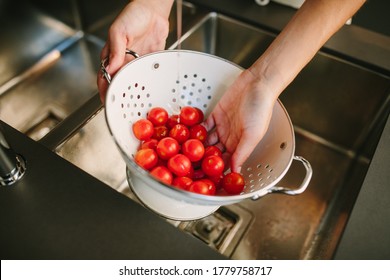 a handful of cherry tomatoes being washed under the tap by a woman - Powered by Shutterstock