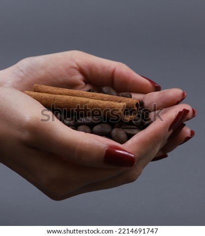 A handful of coffee beans with a cinnamon stick in female hands. Shallow depth of field