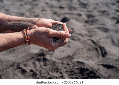 A handful of pouring black sand in female hands on the beach close-up. Falling sand from hands. Black magnetic healing sand. - Powered by Shutterstock