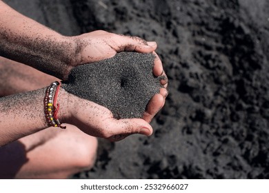 A handful of pouring black sand in female hands on the beach close-up. Falling sand from hands. Black magnetic healing sand. - Powered by Shutterstock