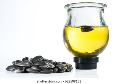 A Handful Of Sunflower Seeds And Sunflower Oil In A Round Glass Jar On A White Background. A Sunflower Seed Is Floating In Sunflower Oil.