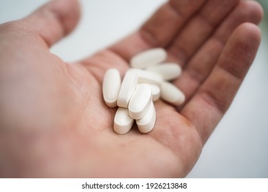 Handful Of White Pills In Male Patients Palm.Healthcare, Treatment, Supplements.Hand Holding Two Aspirin Tablets. Overdose Or Abuse Concept.Young Man Taking Medication, Feeling Ill.