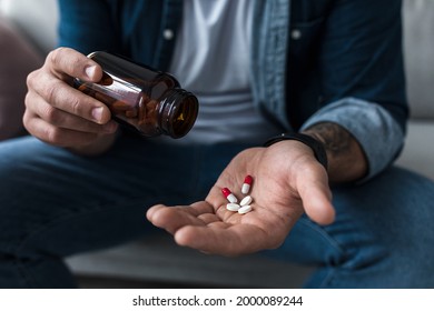 Handful of white pills in male patients palm. Healthcare, treatment, drugs and depression, pain and suicide. Frustrated sad young man holds antidepressants on hand at home interior, close up, cropped