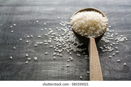 A handful of white polished rice in a wooden old spoon. Dark wood background. View from above. Space for text.