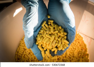 Handful of yellow medical capsules in the hands of a pharmacist on production line pharmaceutical company.