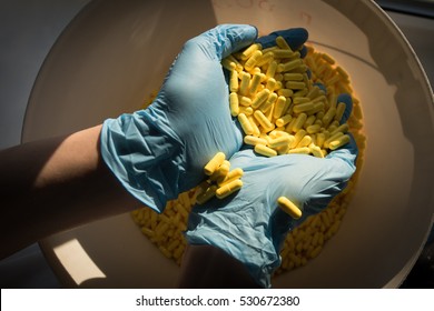 Handful of yellow medical capsules in the hands of a pharmacist on production line pharmaceutical company.