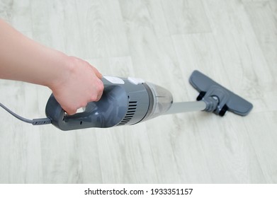 Handheld gray vacuum cleaner in the hand of a Caucasian woman. Vacuum the floor. View from above.