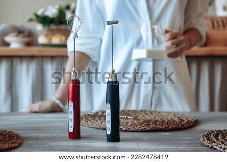 Handheld mixer at woman hands with milk for frother background, making foamy milk. Housewife female at home using mixed cooking food in kitchen. Cooking lifestyle concept. Copy advertising text space