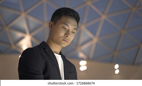 Handheld Portrait Shot Of Young Asian Man Dressed In Jacket And White Shirt Searching For Information In Interactive Wayfinding Kiosk Shot From Below