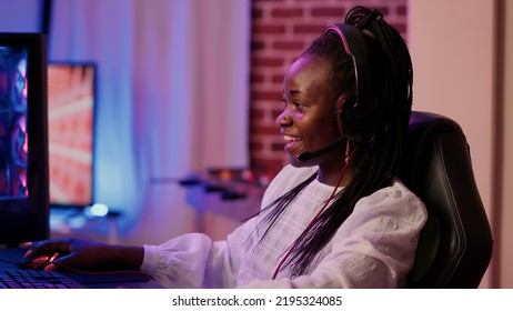 Handheld Shot Of African American Gamer Girl Streaming While Using Gaming Keyboard And Explaining Gameplay. Streamer Talking On Headset While Online Playing First Person Shooter On Gaming Pc Setup.