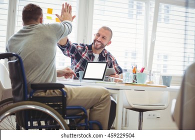 Handicap businessman giving high-five to colleague in creative office