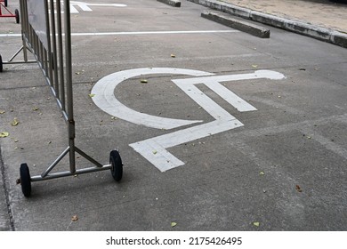 The handicap parking sign is painted white on the road with a steel (stainless steel) traffic barrier and black wheels across. Special parking space reserved for wheelchairs.