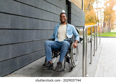 Handicapped accessible city concept. Positive impaired Afro man in wheelchair leaving building on ramp outdoors in autumn, full length. Joyful young black guy using disabled friendly facilities