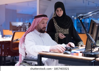 Handicapped Arabic businessman in tradition suit with female arabic assistent working in office. Disabled businessman in the wheelchair works in the office at the computer.