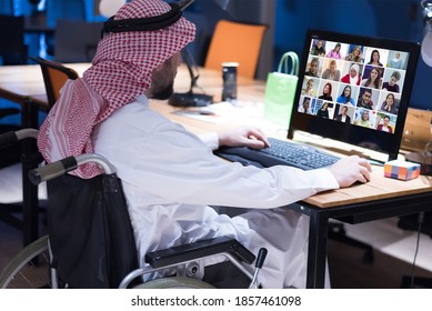 Handicapped Arabic businessman in tradition suit working in office during coronavirus  pandemic. Disabled businessman in the wheelchair works online in the office at the computer.