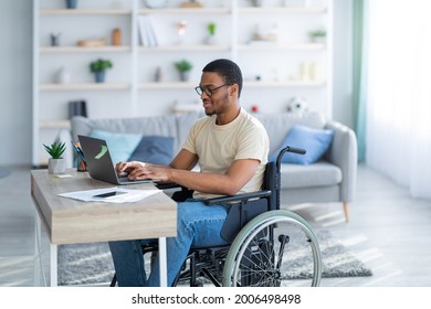 Handicapped Black Guy In Wheelchair Working Online From Home, Using Laptop, Looking For Job Opportunities On Internet. Paraplegic Young Man Having Business Conference, Making Business Project On Web