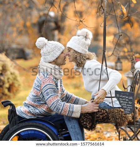 handicapped couple in love, man in wheelchair is kissing his wife in autumn park