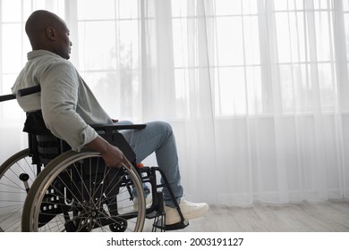 Handicapped Man Sit In Wheelchair In Hospital Or Home, Mature Disabled In Invalid Carriage Or Wheel Chair. Black Male Looks In Large Window With Curtain Background, In Living Room Interior, Profile