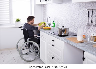 Handicapped Man Sitting On Wheelchair Washing And Cleaning Dishes In Kitchen 