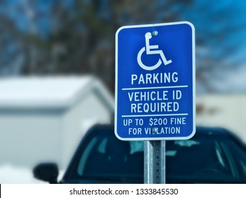 Handicapped Parking Sign With Car, Building And Tree In Snow Covered Parking Lot In Winter. Bokeh Background.