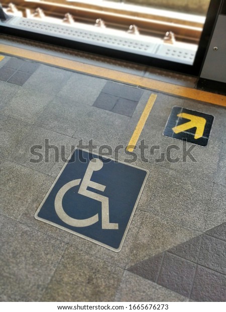 Handicapped\
sign on tile platform, Waiting line for disabled people entrance to\
the train, Behind yellow line for\
safety.