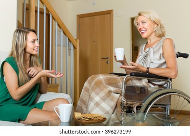 Handicapped smiling woman talking with female guest at the table. Focus on young