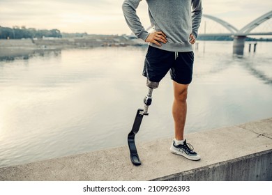A handicapped sportsman with artificial leg standing at the quay with hands on the hips. Legs on the quay.