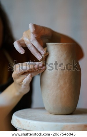 Handicraft art: cropped image of female artisan working with wet clay decorating and shaping jug before baking in pottery studio. Craftswoman creating handmade tableware in workshop creative space.