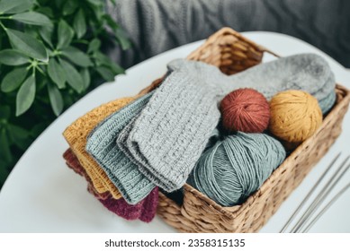 Hand-knitted woolen socks of different colors in a wicker basket on a coffee table close-up