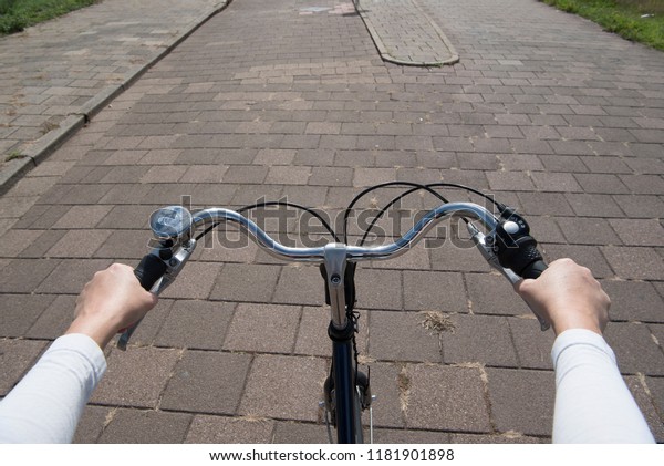 Handle bar on a bicycle seen from the point of view\
of the cyclist with street on the background and hands on the\
steering wheel