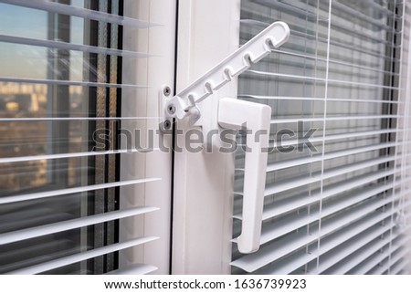 A handle and a restrictor, window stopper or limiter on PVC double glazed window with horisontal aluminium blinds close up.