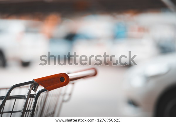 handle of shopping cart and blurred car at parking\
lot, autumn color tone