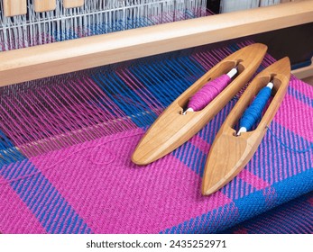 Handloom and shuttles with threads, selective focus. Combination of pink and blue colors. Weaving concept