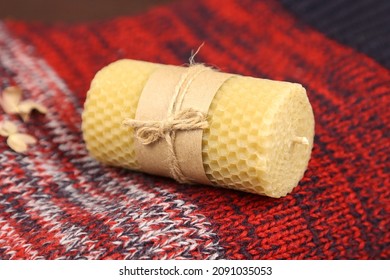 Handmade beeswax candle with craft paper wrapper on Christmas red knitted sweater. Honey aroma for interior and tradition. Mockup, front view.