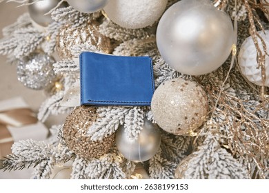 Handmade blue leather wallet on Christmas tree branches, stylish holiday gift idea, festive background with evergreen needles and cozy winter atmosphere, perfect seasonal present
