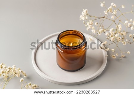 Handmade candle from paraffin and soy wax in glass jar on concrete tray. Candle making. Minimalism. Luxurious white tray decoration, home interior decor with burning aroma candle with white dry flower