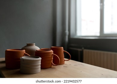 Handmade Ceramic Craft Ware - Empty Cups And Bowls On A Wooden Table In Front Of Window In Pottery Studio. Space For Text