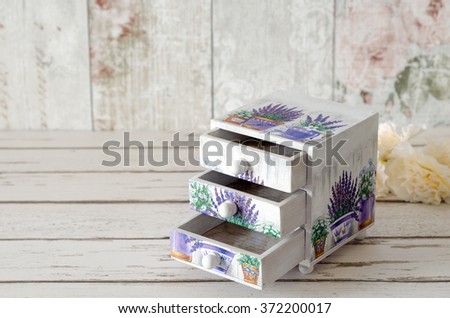 A handmade chest of trinket drawers decoupaged with vintage paper with pots of Lavender on a rustic wooden background