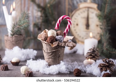 Handmade chocolate candies and candy cane in paper pot on wooden table with Christmas and New Year decor. Background decoration with vintage weight scales, candles, pine cones, branches and fake snow - Powered by Shutterstock