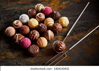 Handmade chocolate praline bonbon display with a neat rectangle of assorted fondants on rustic wood with wire lifter and fork
