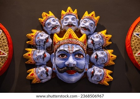 Handmade colorful tribal look of Ravan face mask souvenir hanging on plain black background. Selective focus on object.