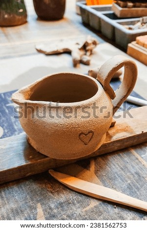 Handmade creamer. A small earthenware jug. A clay jug on a tray before the firing process at high temperature in the furnace at the factory. Pottery workshop. Selective focus.
