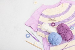 Handmade Crocheted Baby T-shirt In Lilac Tones. Stuff And Props Contains Thread, Hooks, Knitting Needles And Craft Decor. Light Stone Concrete Background, Top View