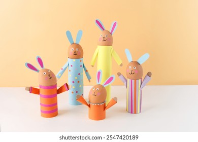 Handmade Easter bunny crafts using colored paper and eggs on a peach background. holder made of recycled toilet paper roll. Easter celebration and DIY craft concept. soft focus