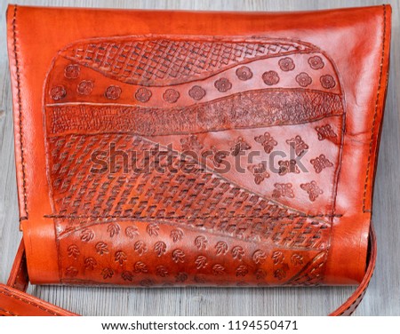 handmade embossed pattern on back side of orange colored leather handbag on gray wooden table